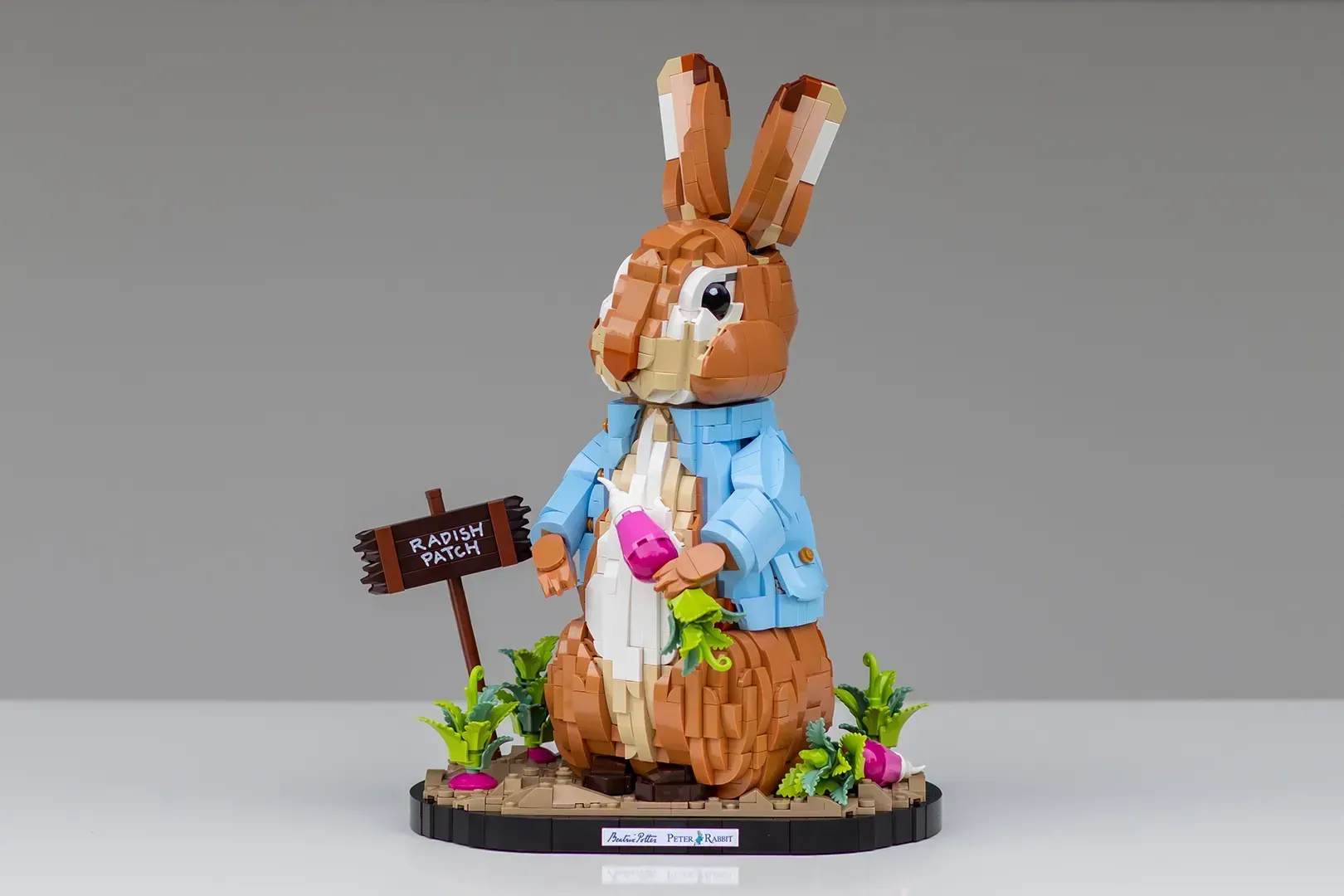 LEGO Ideas Peter Rabbit set featuring brown rabbit in blue jacket holding radish, standing in garden base with sign.