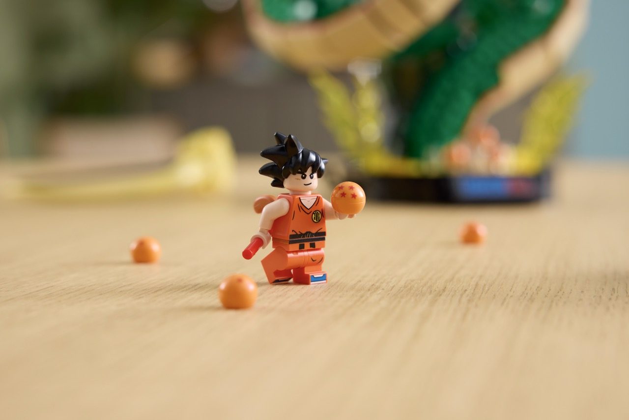 LEGO Goku minifigure in orange gi holding a Four-Star Dragon Ball, surrounded by orange spheres on wooden surface.