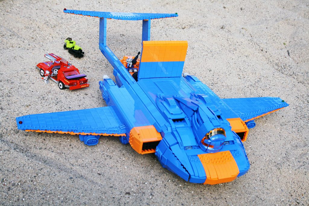 LEGO M.A.S.K. blue aircraft playset with orange accents, minifigure, and toy vehicles on concrete.