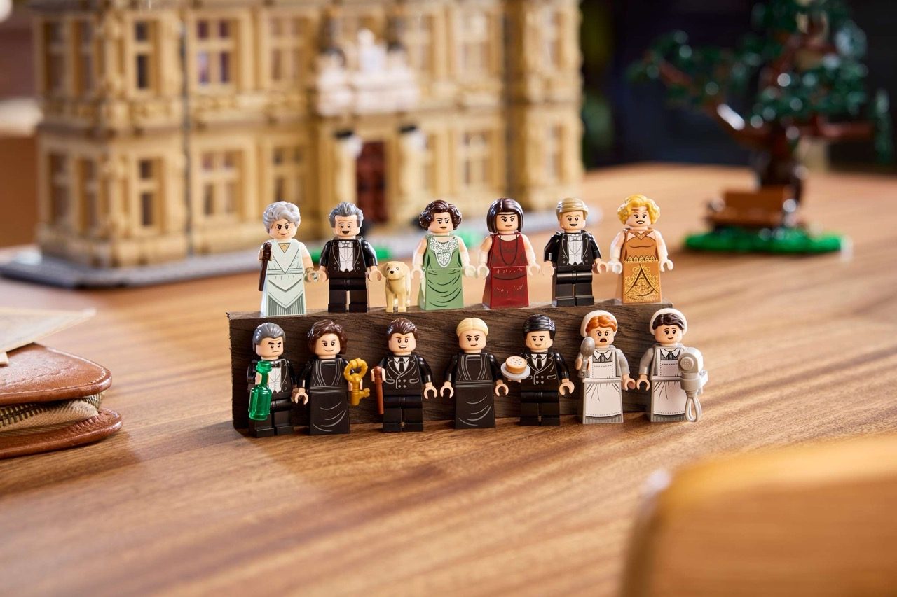 LEGO Downton Abbey minifigures arranged on wooden surface with Highclere Castle set in background.