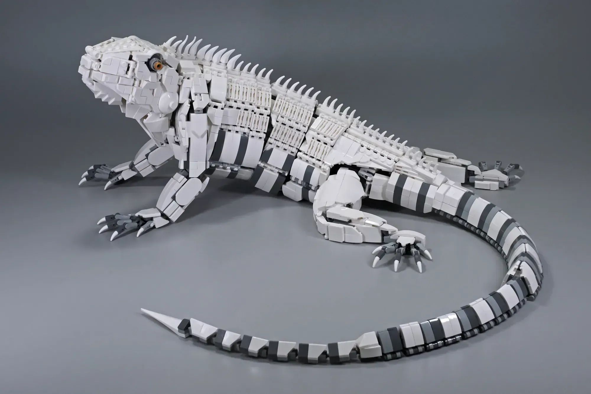 White and gray LEGO robotic lizard with segmented body and articulated tail on gray background.