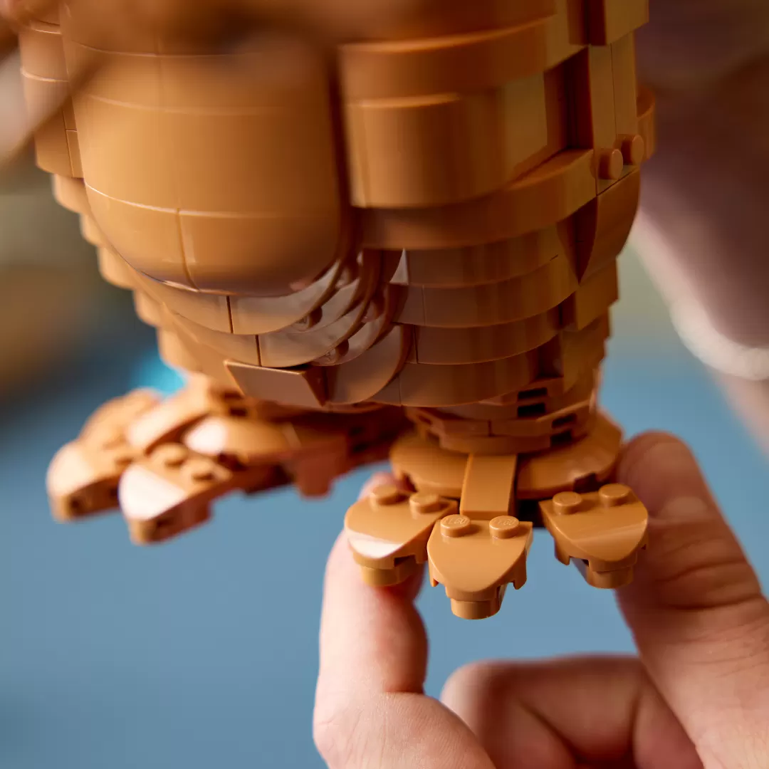 LEGO E.T. figure held in hands, tan brick construction with glowing heart piece, blue background.