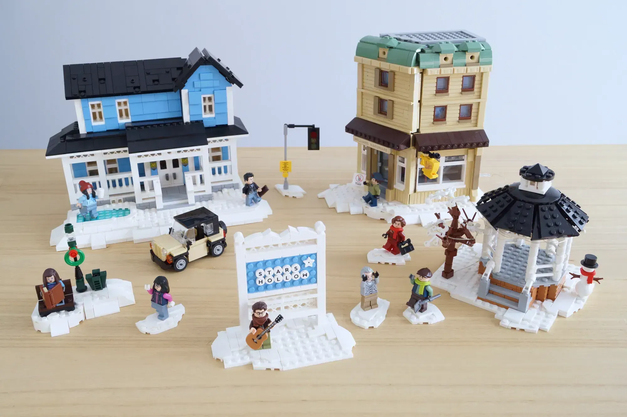 LEGO winter town scene with blue and cream house, tan apartment building, gazebo, minifigures, snow base plates, and acces…