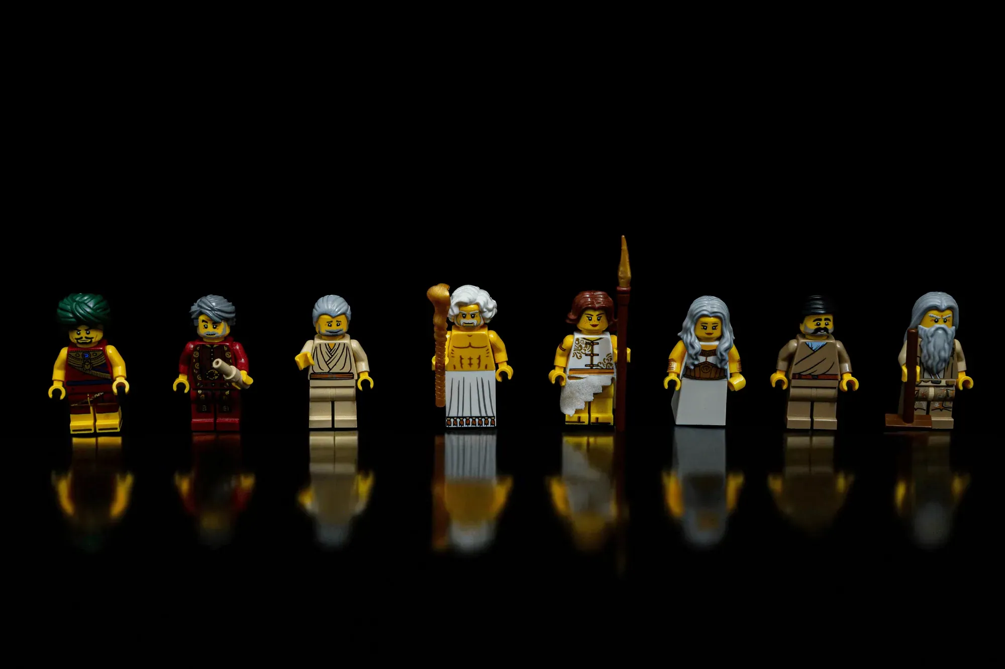Eight LEGO minifigures in historical Greek and Egyptian attire lined up against a black background with reflections.