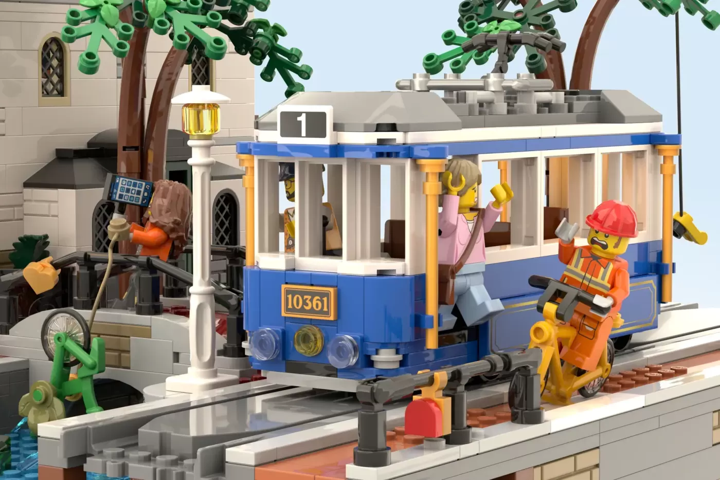 Blue and yellow LEGO tram numbered 10361 at station with minifigures, trees, and canal-side Amsterdam-inspired buildings.