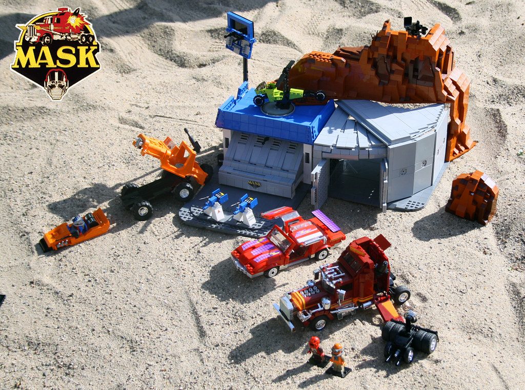 M.A.S.K. LEGO set featuring blue command base, red vehicles, orange equipment, minifigures, and sand terrain display.