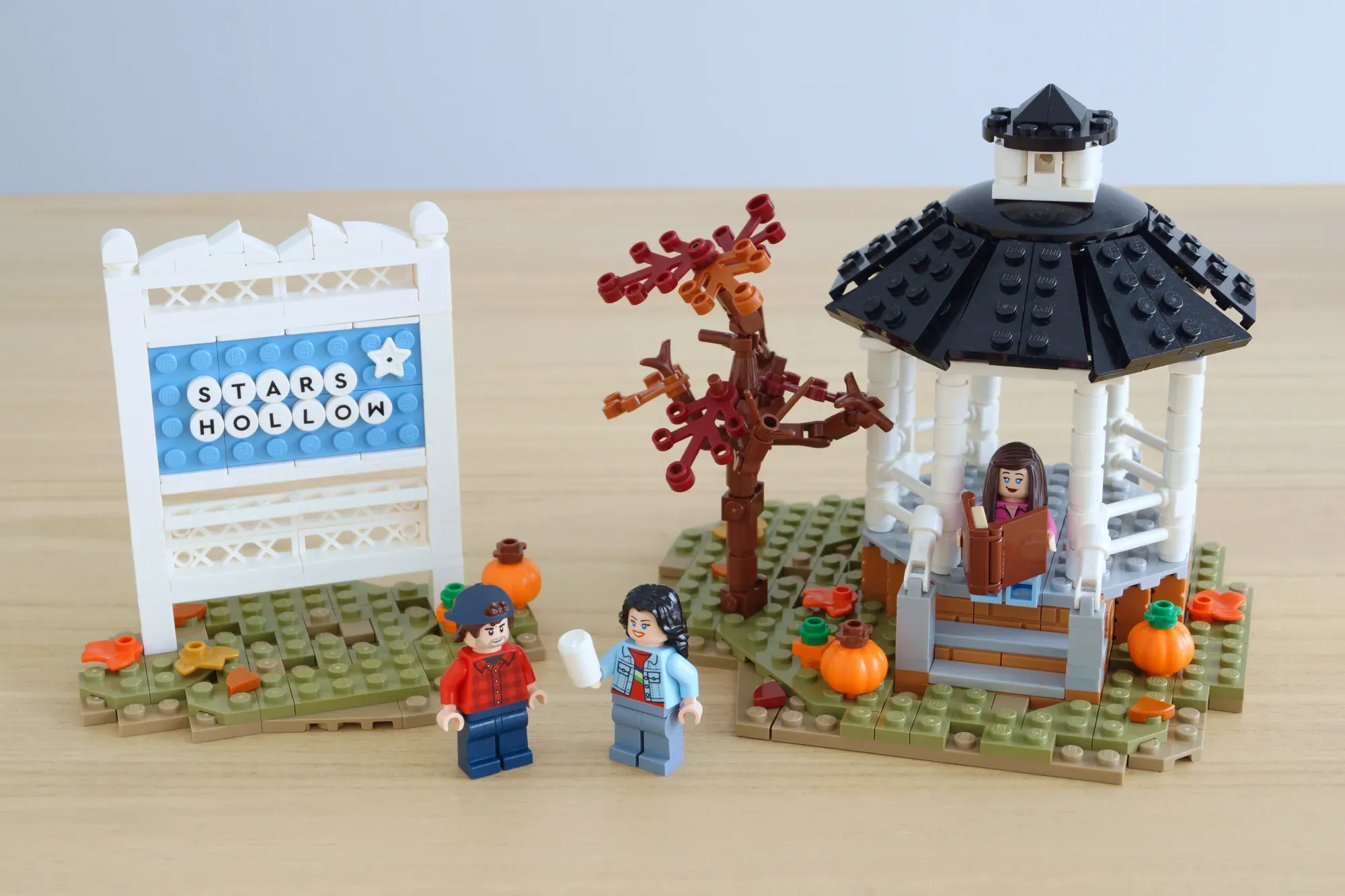 LEGO Stars Hollow set with minifigures, gazebo, tree, pumpkins, and Luke's Diner sign on wooden surface.
