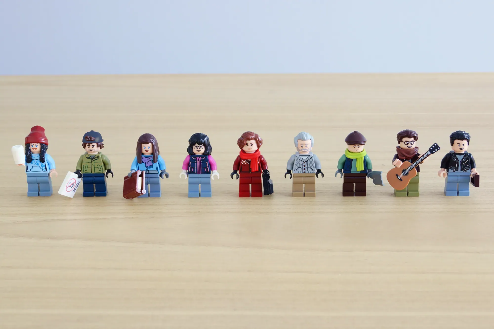 Nine LEGO minifigures from Gilmore Girls lined up on a wooden surface against a light blue background.