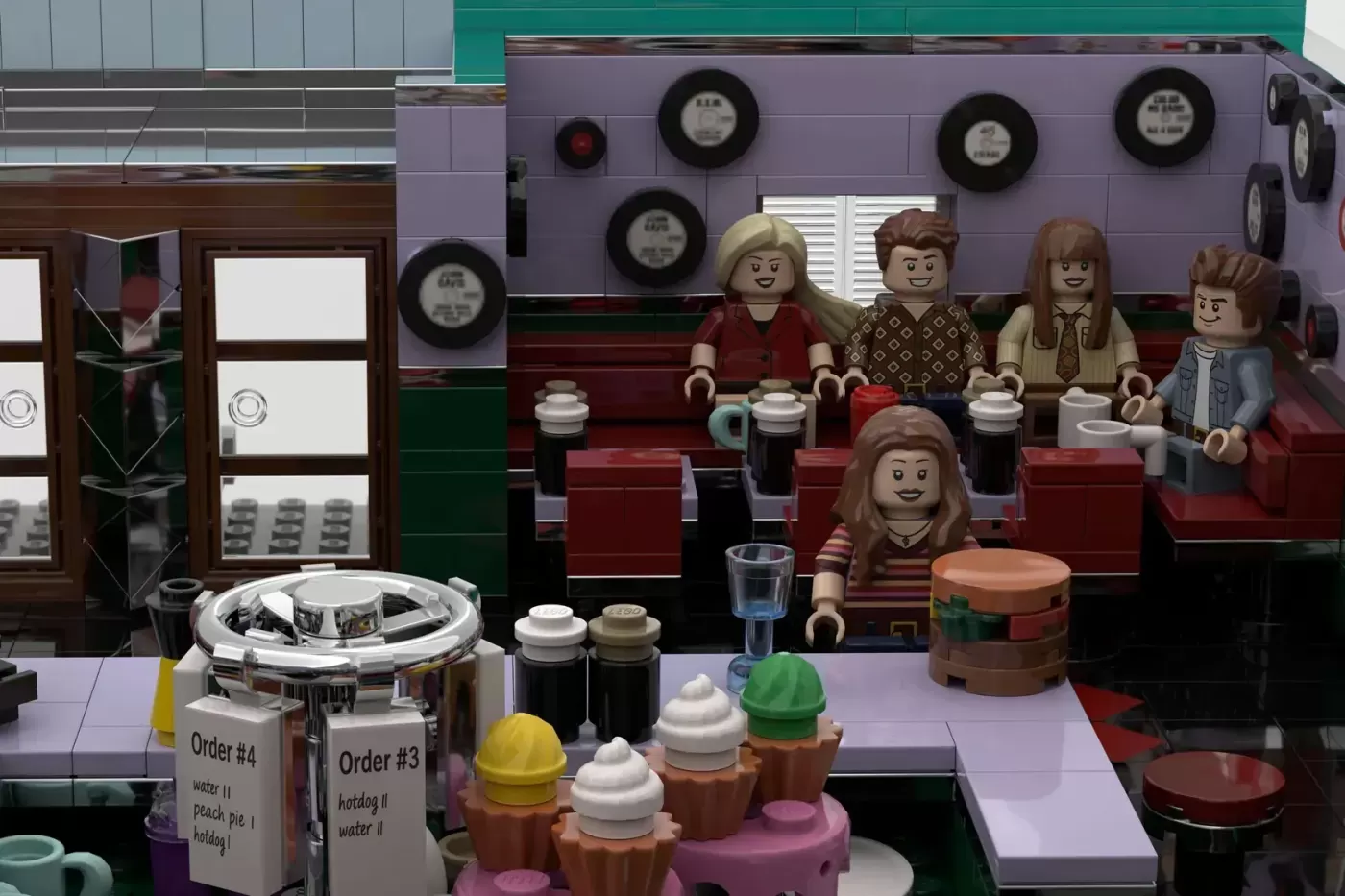 LEGO Peach Pit diner set with six minifigures seated at booths, counter with cupcakes, clocks on walls, and detailed inter…