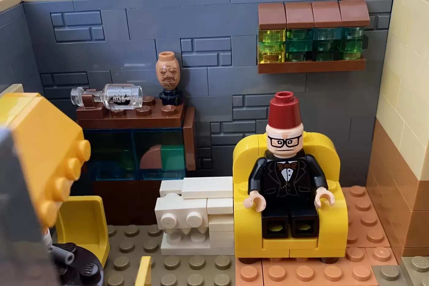 LEGO MOC of Gravity Falls Mystery Shack interior with minifigure in yellow chair and desk accessories.