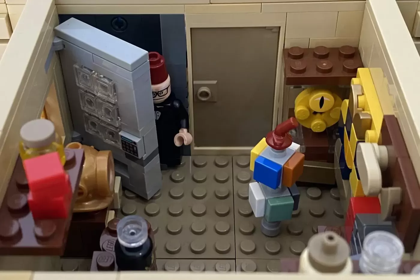 LEGO Mystery Shack interior with minifigure, computer, furniture, and colorful accessories on tan baseplate.