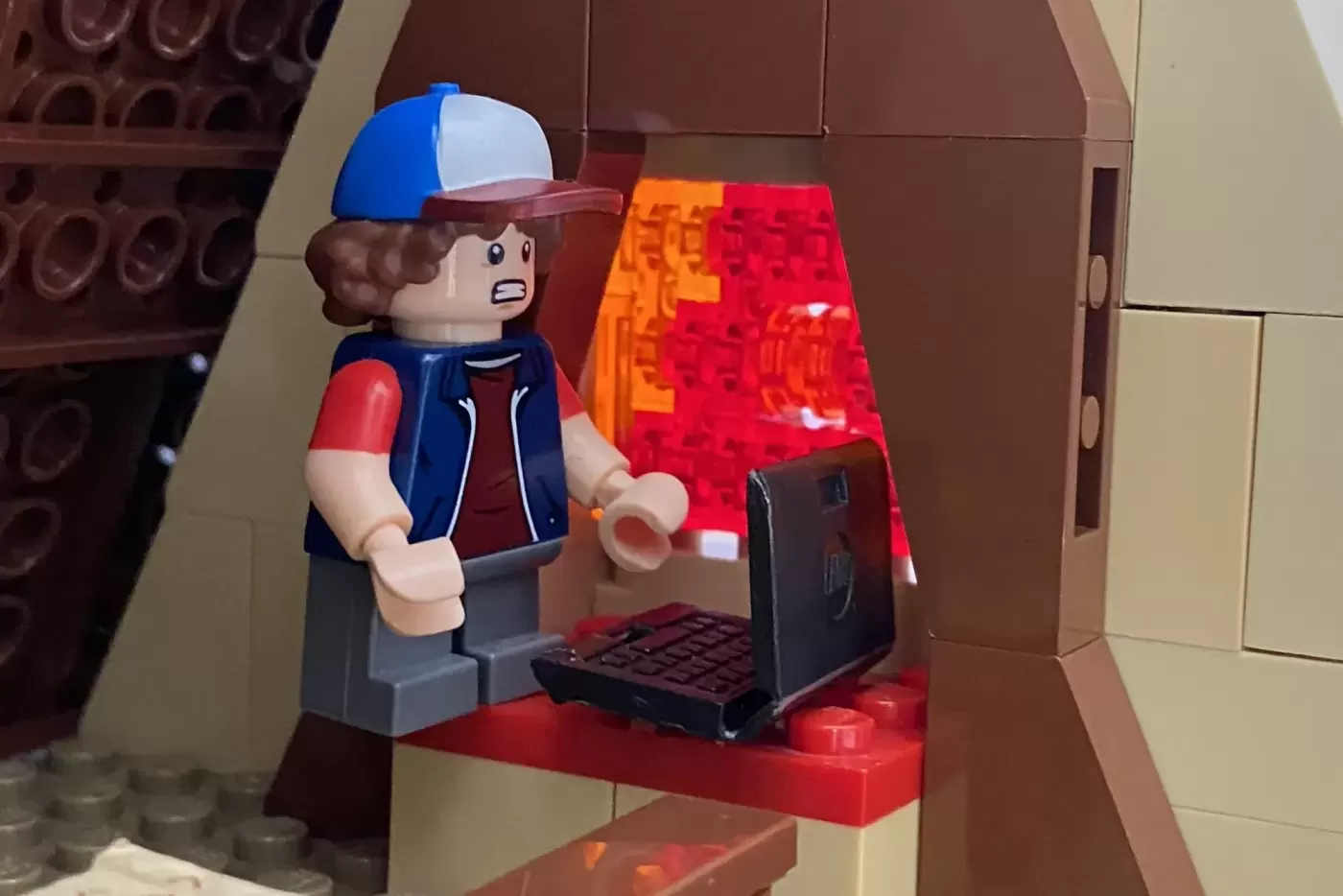 LEGO minifigure in baseball cap working at computer desk inside brown Mystery Shack building model.