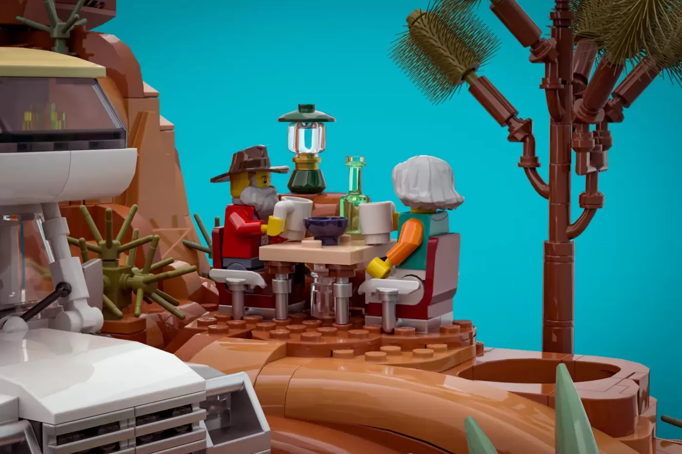 LEGO retirement scene with two minifigures dining at a desert table, camping gear, lantern, and RV against turquoise sky.