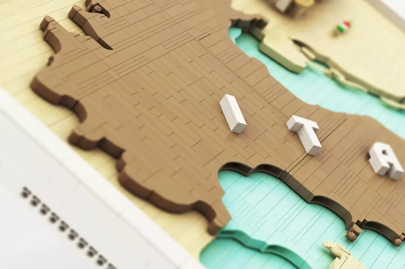 3D LEGO brick map of Italy with tan landmass, turquoise water, and white minifigure accessories on tan baseplate.
