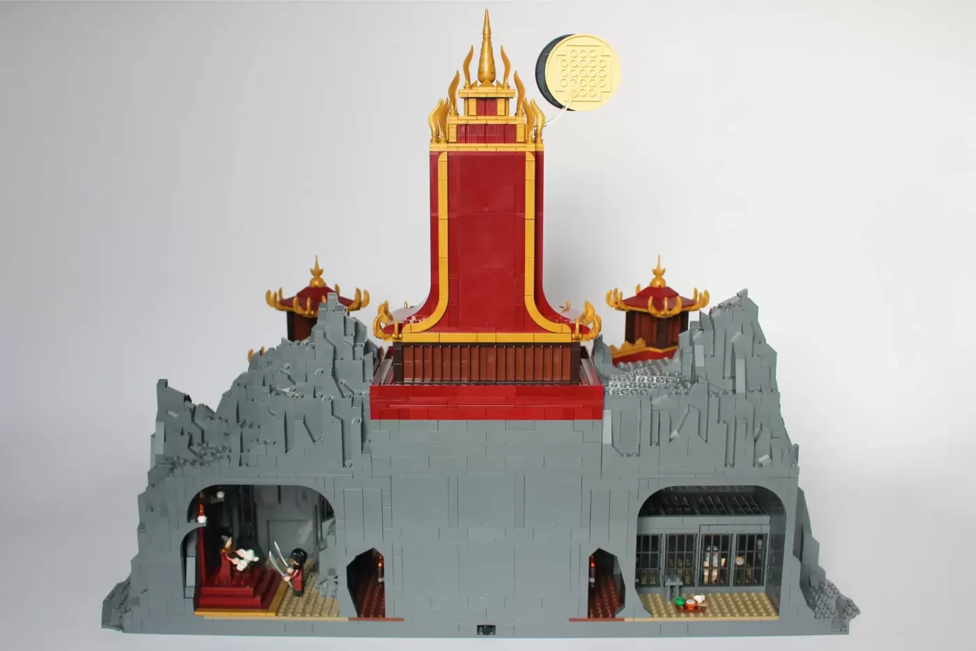 LEGO Fire Nation Palace with golden spires, red walls, grey stone base, two side pavilions, and minifigures visible inside.
