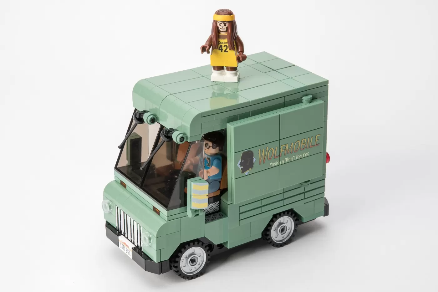 LEGO Wolfmobile set with minifigure driver and basketball player on roof, sage green vehicle with windshield and wheels.