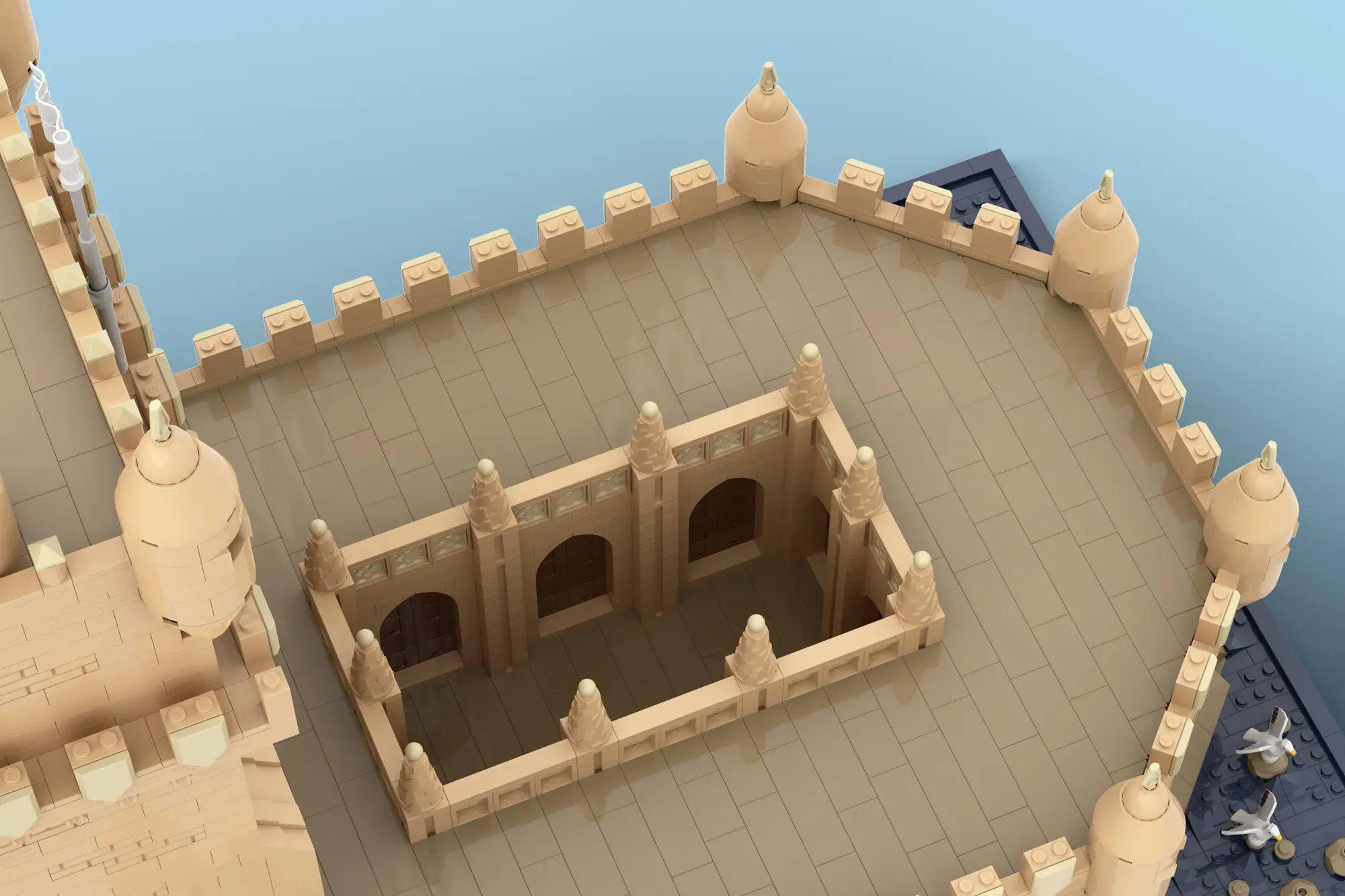 LEGO Belém Tower model showing tan castle courtyard with arcaded structure and corner turrets against blue backdrop.